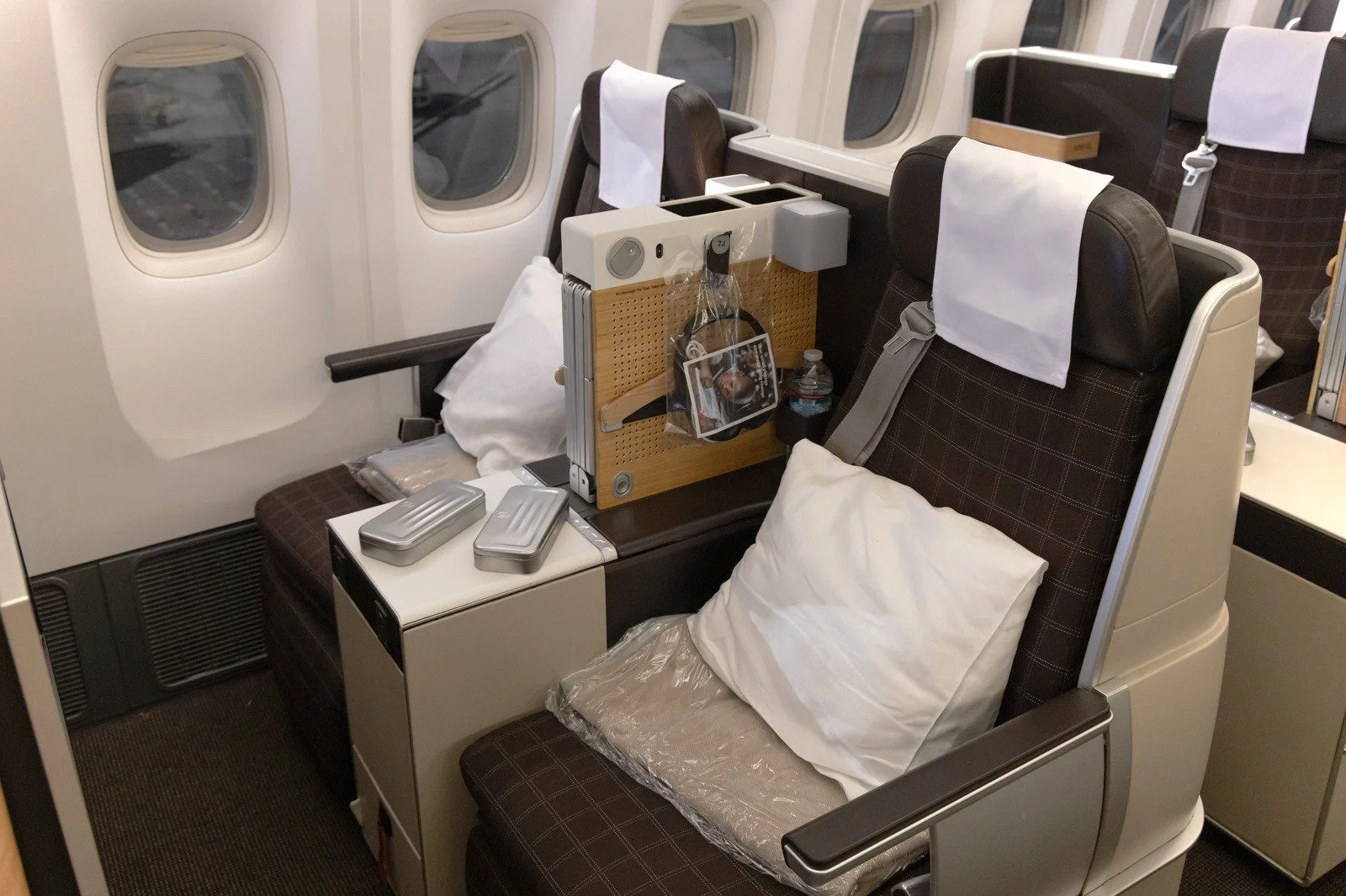 Business-class seat with a pillow and blanket beside the windows of a wide-body airliner
