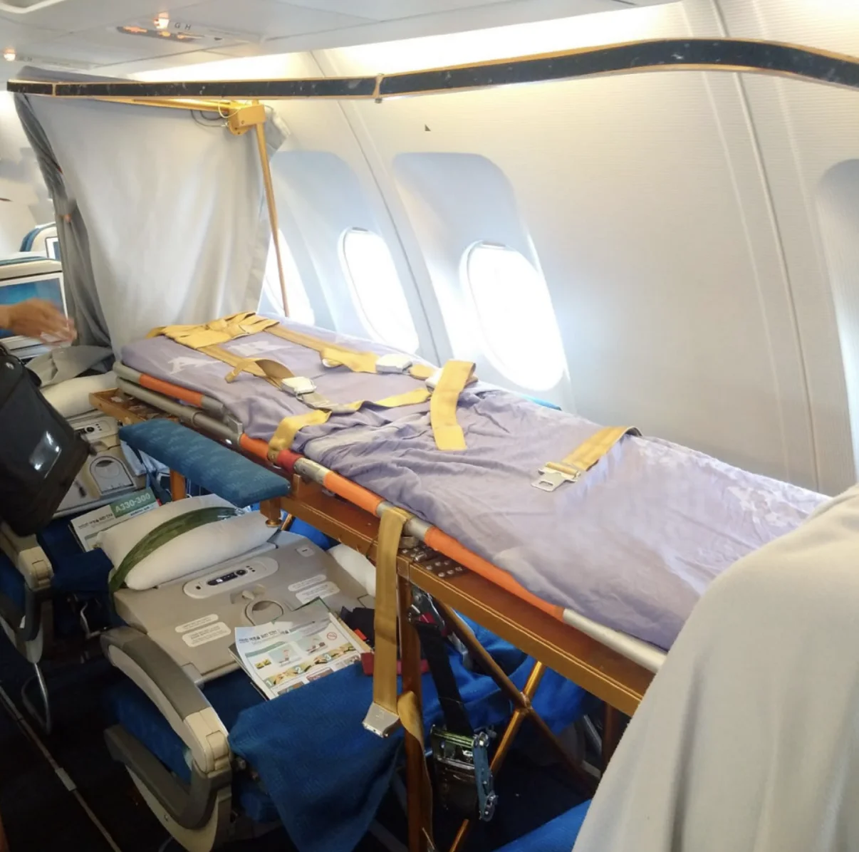 Medical stretcher fitted over a row of economy seats beside the windows of a commercial airliner
